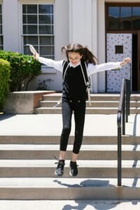 Joyful girl jumping on school steps in sunny weather, symbolic of education and happiness.